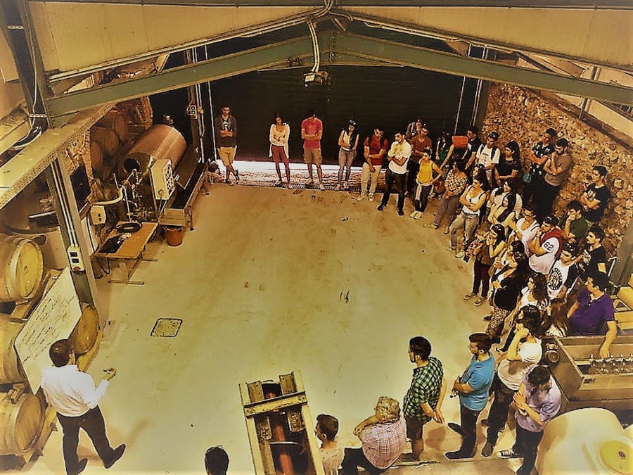 guide presenting tourists the Nikolou Winery plant in front of grape press machine